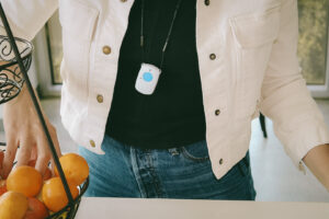 Woman shown from chest to hips wearing a fall detection device on lanyard in a kitchen setting